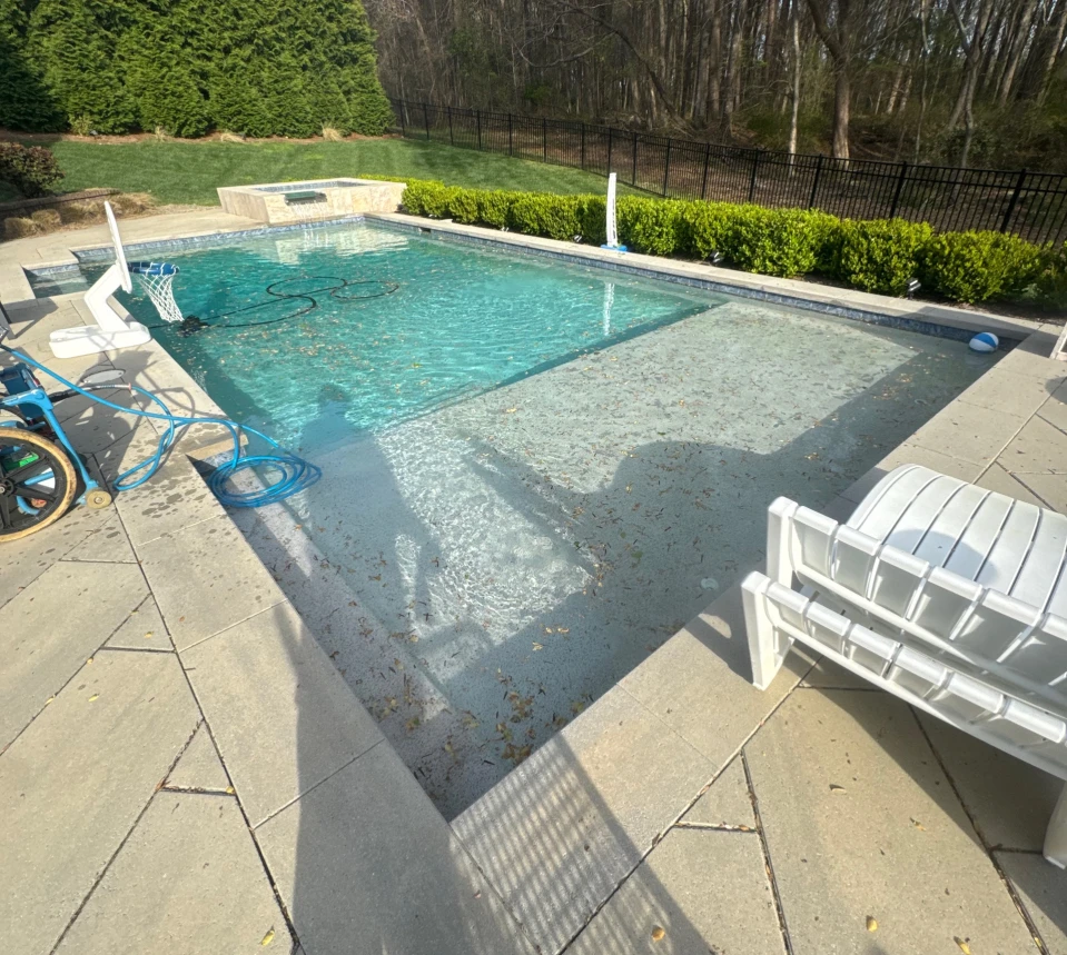 A pool with a basketball hoop on the left, a dirty shallow end, and a clean deep end